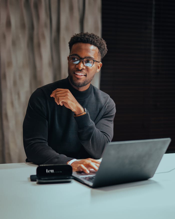 Mastering the First Impression: Your intriguing post title goes here Cheerful man with glasses working on laptop at a table indoors, emanating a professional and modern workspace vibe.